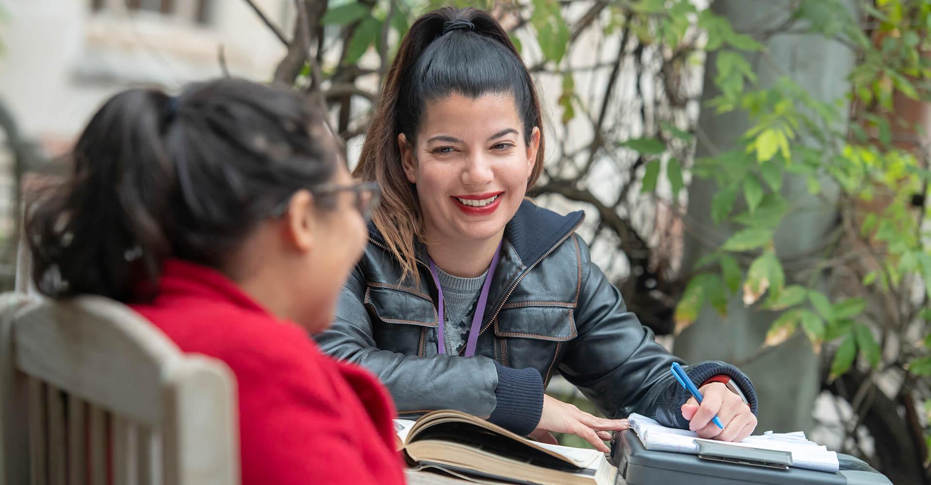 Two students engaged in conversation while studying outside.